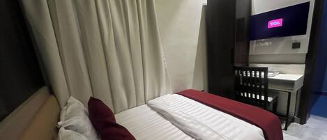A hotel room with a bed, a desk, a chair, a TV, and an air conditioning unit.