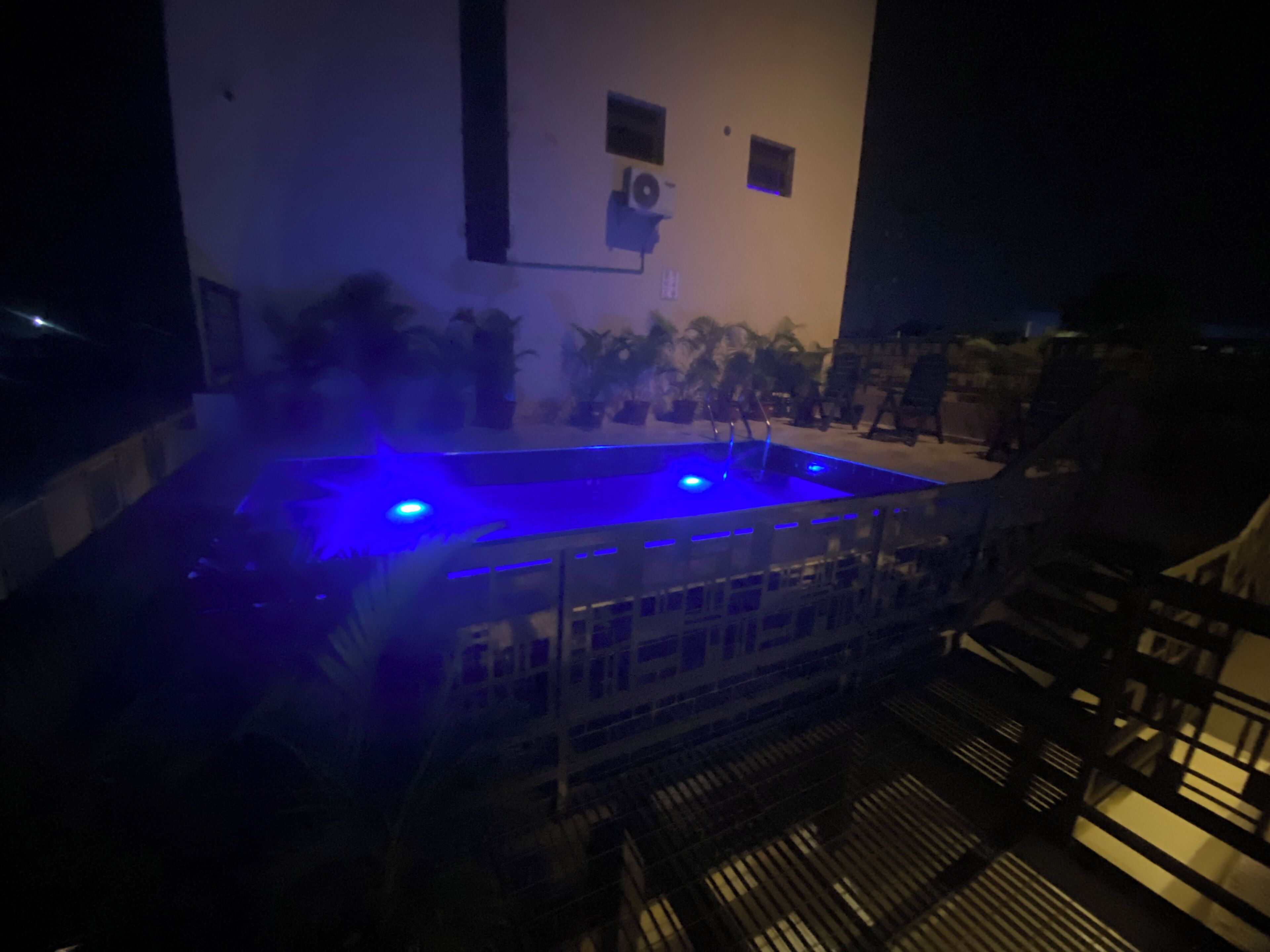 Una piscina con iluminación azul, rodeada por un edificio con numerosas ventanas y una escalera.