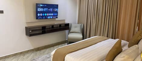 Una habitación de hotel moderna con cama, televisor montado en la pared, una silla y cortina.