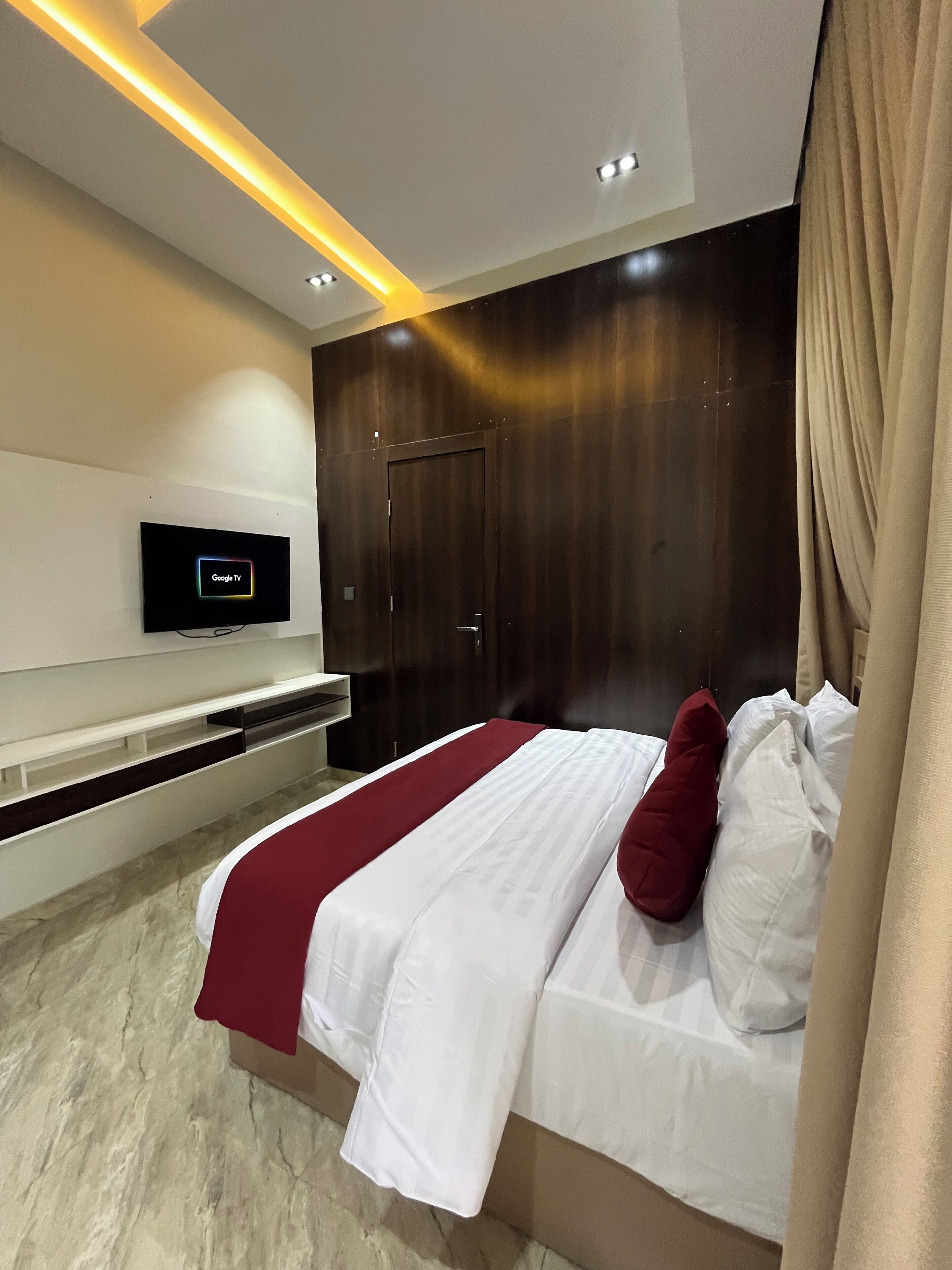 A modern hotel room with a bed, a mounted television, and a wooden wardrobe.