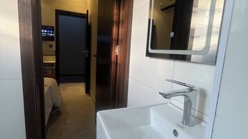 Un baño moderno con un lavamanos blanco, un espejo y una puerta que da a un pasillo.