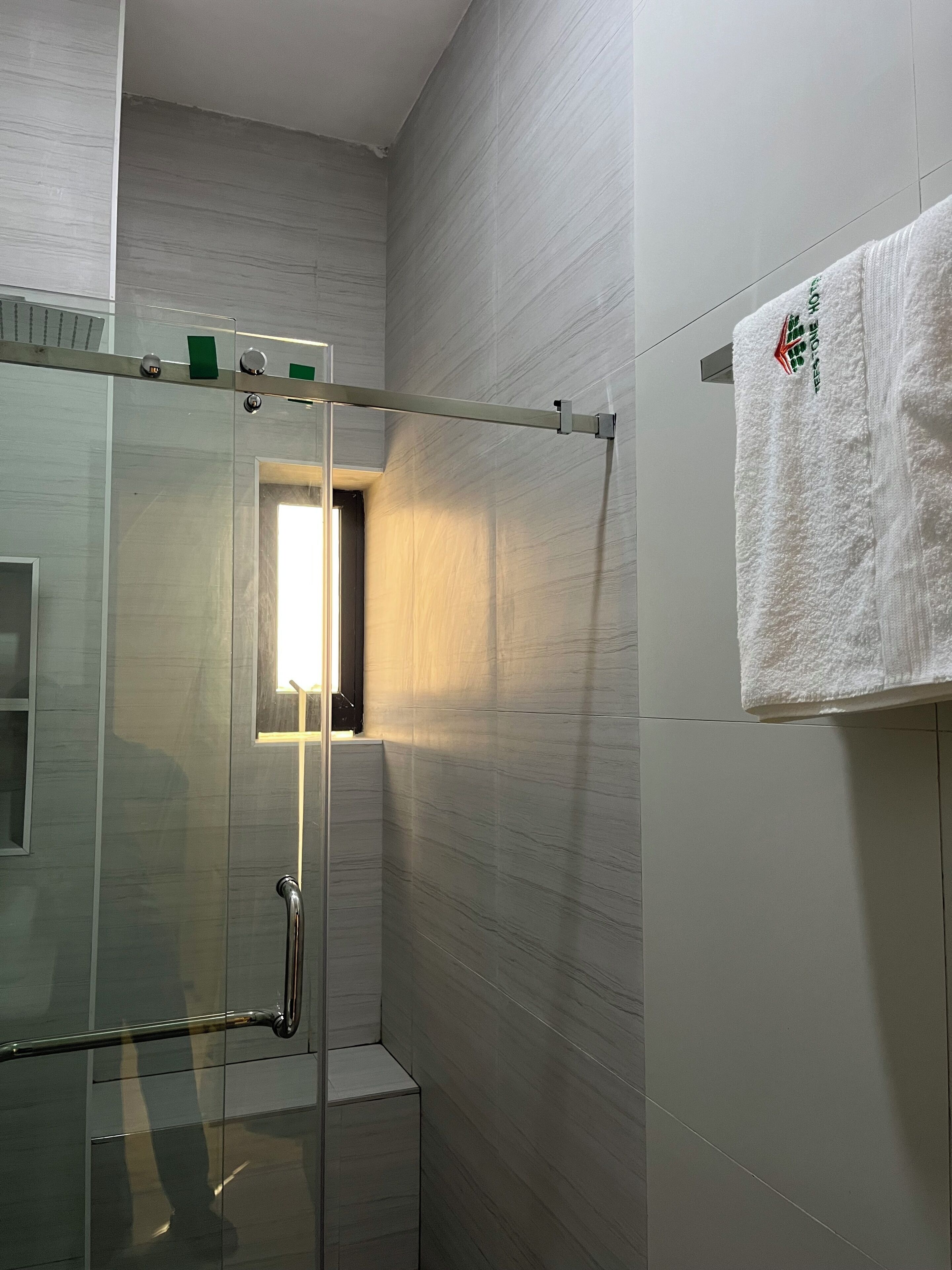 A modern bathroom with a glass shower enclosure, a towel hanging on the wall, and a visible door leading to another room.