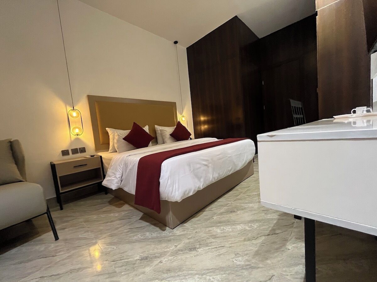 A modern hotel room with a bed, bedside table, lamp, and a large mirror.