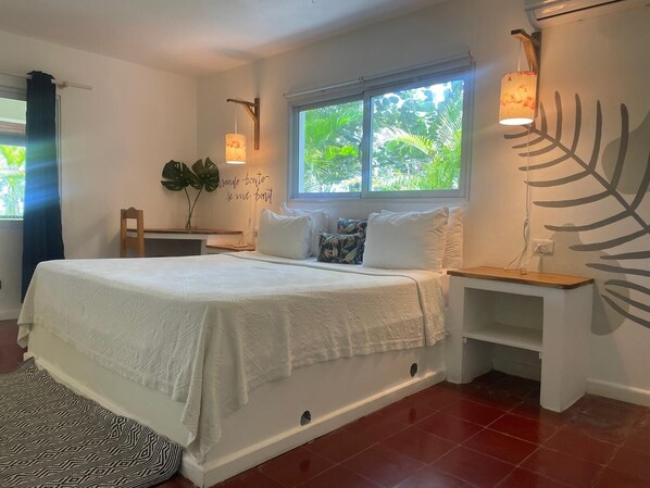 A bedroom with a bed, bedside tables, a window with a view of greenery, a wall-mounted lamp, and a decorative plant. - Hotel Boutique Casa Grande Playa Bonita (Las Terrenas)