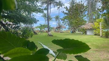 Un jardín tropical con palmeras, una cabaña de techo de paja y un césped.