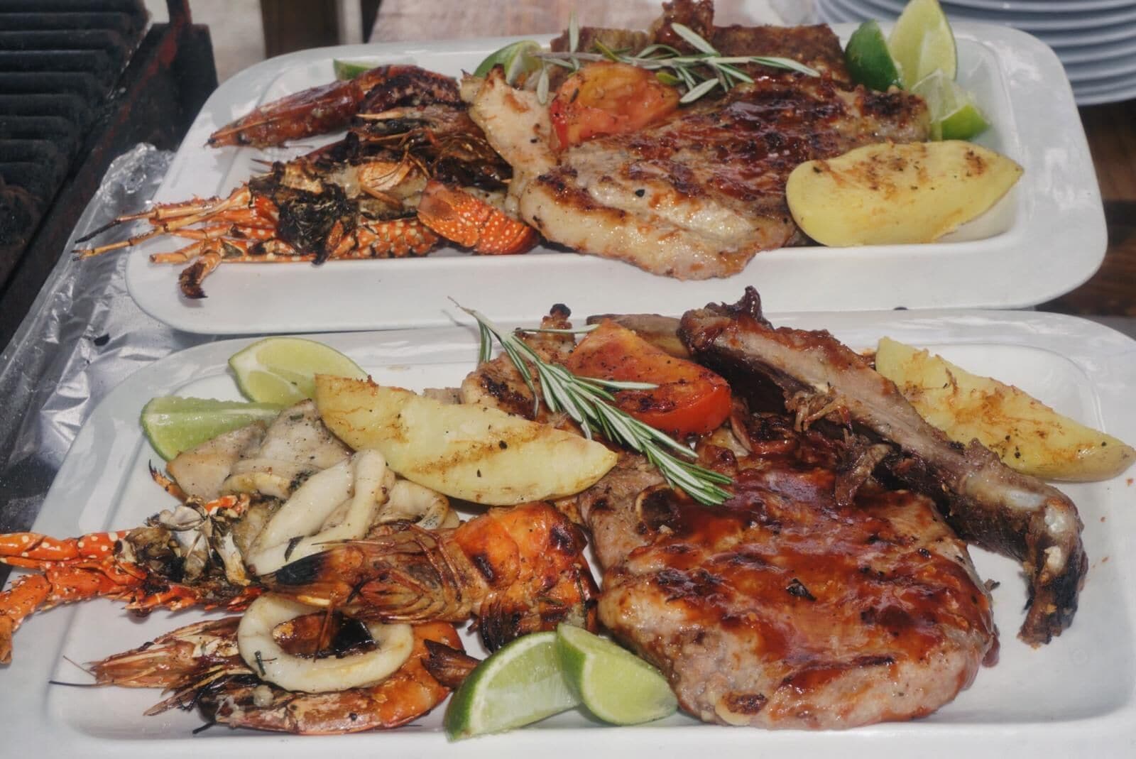 Un plateau de fruits de mer comprenant des crevettes grillées, du homard et un steak, agrémenté d’herbes et de citron vert.