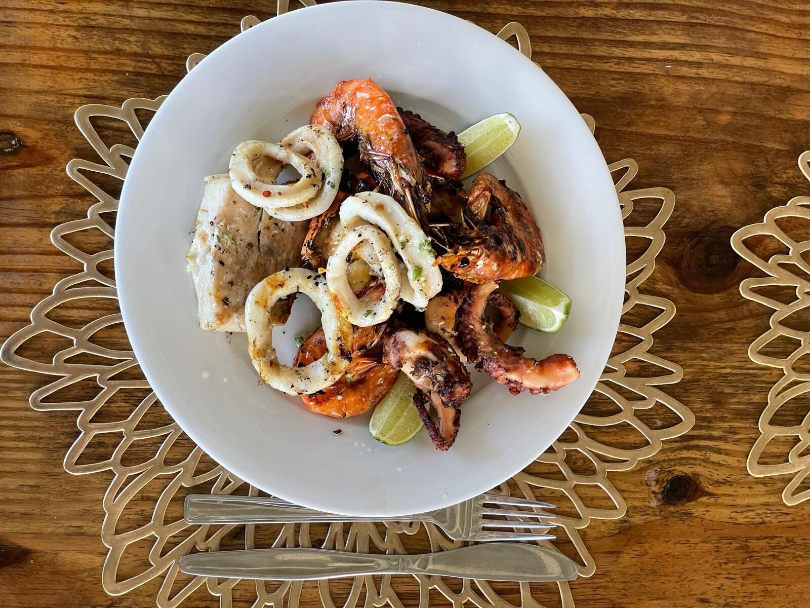 A plate of grilled shrimp and squid rings on a white plate with a decorative doily underneath.