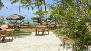 A beachside dining area with tables and chairs, a view of the ocean, and palm trees. - Hotel Boutique Casa Grande Playa Bonita (Las Terrenas)