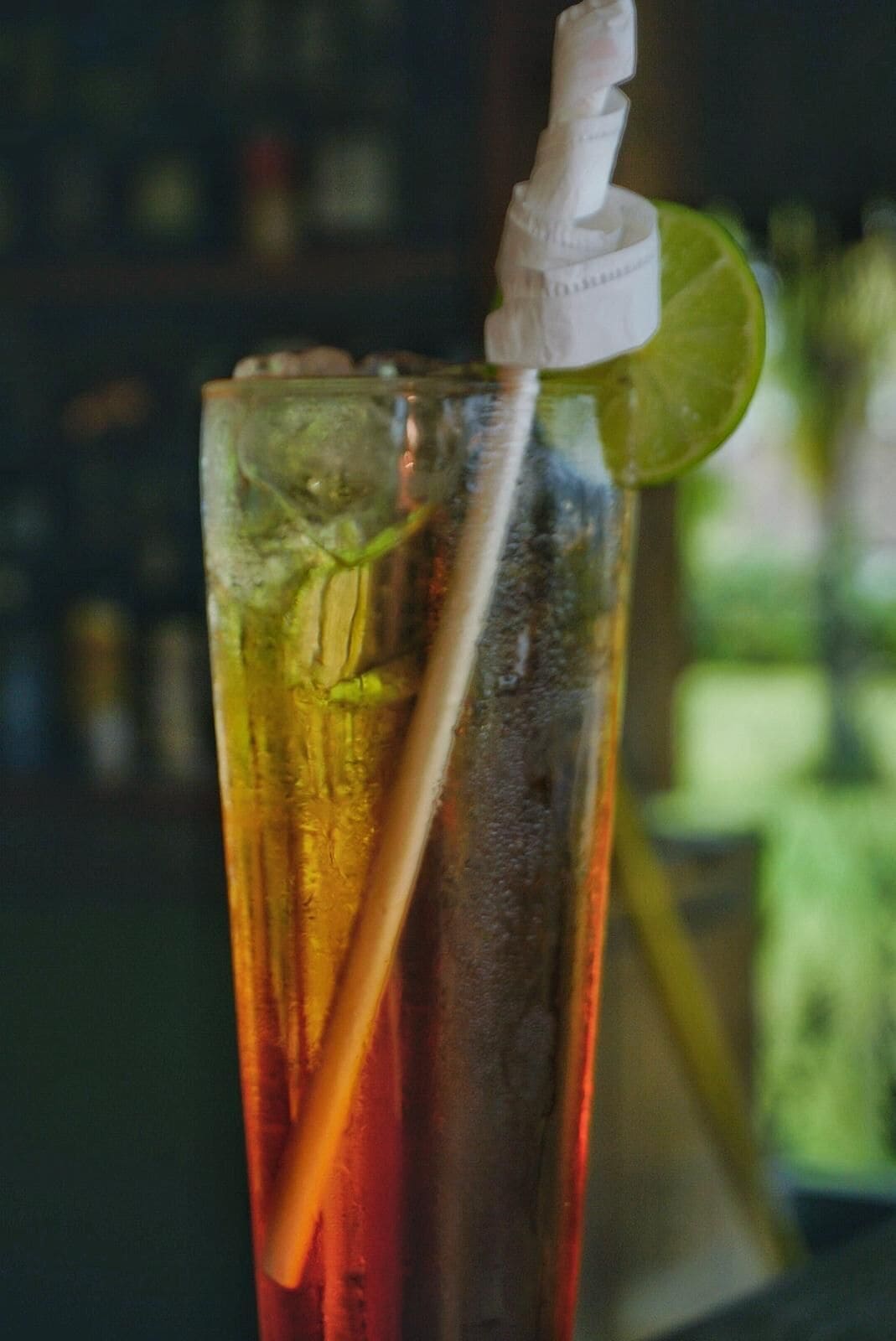 A tall glass with a straw and a lime wedge, containing a red beverage, possibly iced tea, with ice cubes.