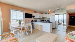 Una cucina compatta con mobili bianchi, un'isola centrale e una zona pranzo con sedie bianche.
