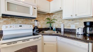 Una cucina compatta con piano cottura, forno a microonde, lavastoviglie e macchina per il caffè.