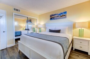 A bedroom with a large bed, a nightstand, a bedside table, a mirror, and a painting on the wall. - Oceanfront condo in Carolina Beach, perfect for a relaxing getaway 0607 (Carolina Beach)