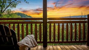 Una terraza de madera con vista a una puesta de sol sobre un paisaje boscoso.