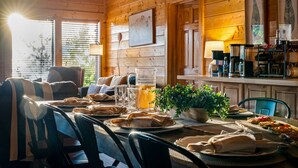 Interior de una cabaña de madera con una mesa de comedor preparada para una comida, una jarra de cerveza y una planta en maceta.