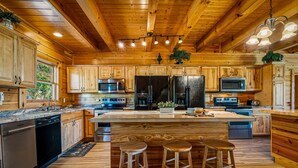 Una cocina de estilo cabaña de madera con electrodomésticos integrados, una isla grande con taburetes y un techo rústico.