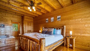 Un dormitorio de cabaña de madera con una cama, cabecero de madera, ventilador de techo, mesita de noche y una ventana.