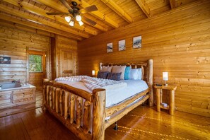 Ein Schlafzimmer einer Holzhütte mit einem Bett, einem Holz-Kopfteil, einem Deckenventilator, einem Nachttisch und einem Fenster.