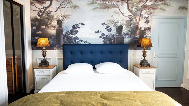 A bedroom with a large bed, two nightstands, a blue headboard, and a mural of trees and a sea view on the wall. - Charming manor house in Brittany (Binic-Étables-sur-Mer)