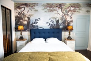 Un dormitorio con una cama grande, dos mesitas de noche, un cabecero azul y un mural con árboles y vistas al mar en la pared.