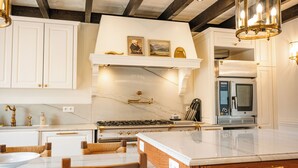 A kitchen with white cabinetry, a marble countertop, a stove, a microwave, and a hanging light fixture. - Charming manor house in Brittany (Binic-Étables-sur-Mer)
