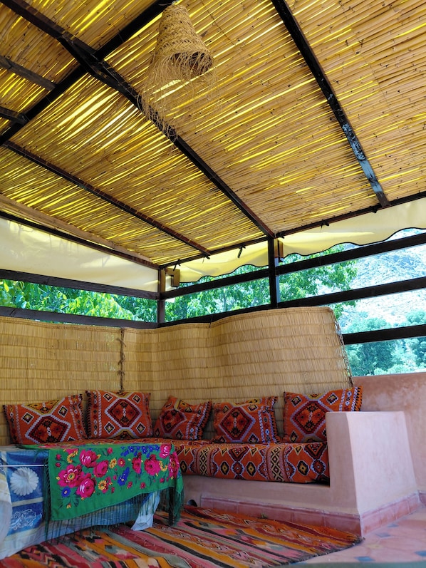 A room with a thatched roof, a woven bench, and a view of greenery outside.