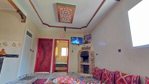 A living room with a TV, a fireplace, a red door, and a patterned rug.