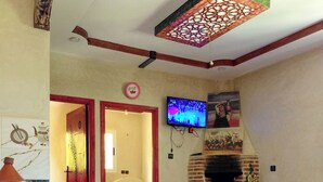 Uma sala de estar com televisão, lareira, tapete estampado e piso de mármore.