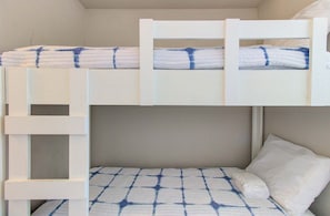 Ein Etagenbett mit einer Stehle, ein Bett mit gemustertem Bettbezug und ein Kopfkissen.