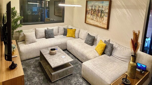Una sala de estar moderna con un sofá modular, una mesa de centro, un televisor y un cuadro en la pared.