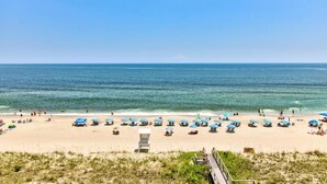 A beach with umbrellas and people, a clear sky, and the ocean. - Seaside serenity awaits at 0609 Oceanfront Escape in Carolina Beach! (Carolina Beach)