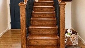 A wooden staircase with black railings, a dark door, and a basket with towels and a dog statue. - Makua Jim’s - Quiet Cove Retreat with Swim Dock, 3 Decks, boat slip, & game room (Sunrise Beach)