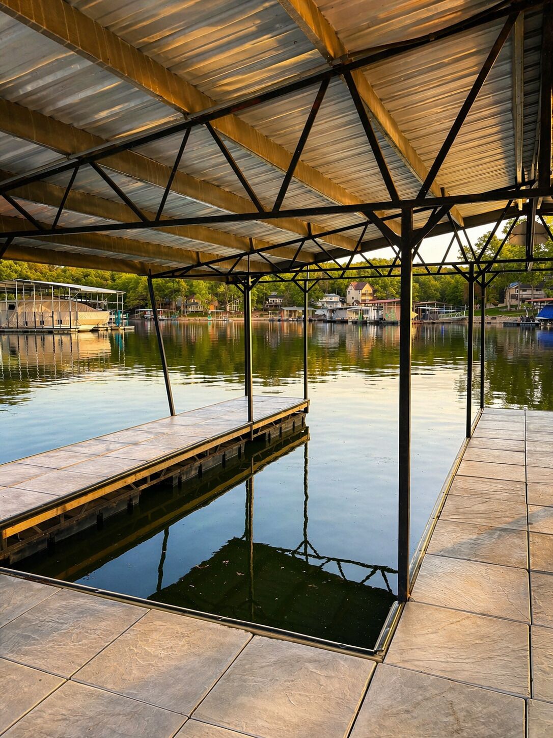 A covered dock extending into calm water with a clear view of houses in the background.