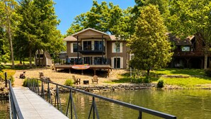 A dock extending into a lake with a house in the background. - Makua Jim’s - Quiet Cove Retreat with Swim Dock, 3 Decks, boat slip, & game room (Sunrise Beach)