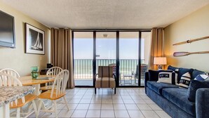 A room with a dining table, chairs, a sofa, a TV, a framed picture, and a balcony with a view. - Breathtaking oceanfront views await at 0610 Smooth Sailing in Carolina Beach. (Carolina Beach)