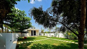 A backyard with a lawn, a small building, and a white wall. - Rewind by Nestora Homes (Private luxury cottage) (Byranahosahalli)