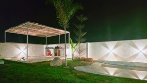 A covered outdoor area with a concrete floor, surrounded by a white wall with geometric patterns, and a small tree in the center. - Rewind by Nestora Homes (Private luxury cottage) (Byranahosahalli)