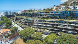 Ein modernes, mehrgeschossiges Hotel mit Dachgärten, Blick auf die Küste und einer Mischung aus Wohn- und Geschäftsgebäuden im Hintergrund.