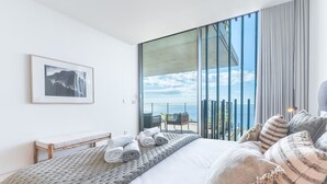 Ein modernes Schlafzimmer mit großem Bett, Meerblick und einem Balkon mit Tisch und Stühlen.