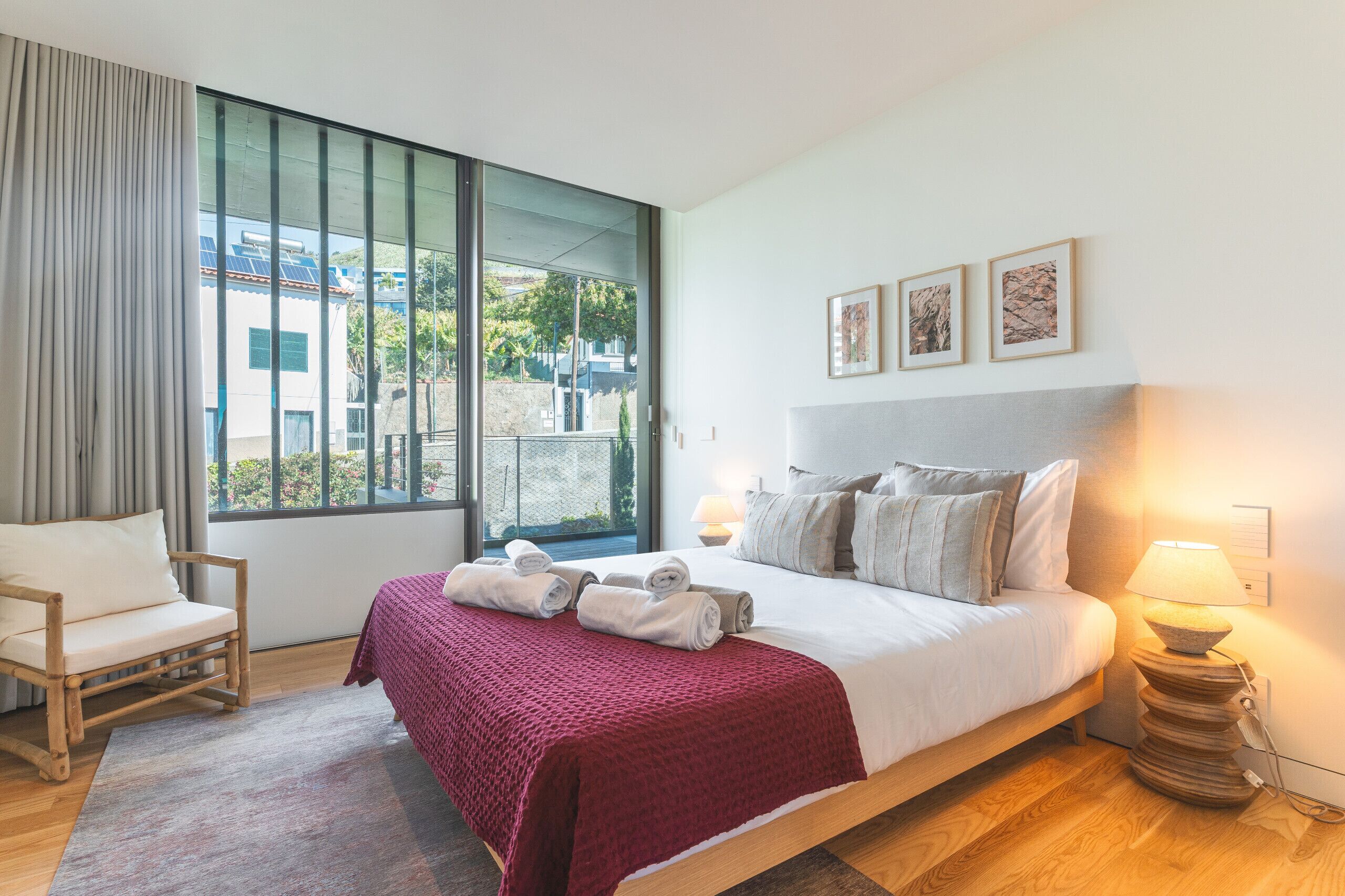 Une chambre d’hôtel avec une grande fenêtre, un lit avec des oreillers et des serviettes, une chaise et une table de chevet avec une lampe.
