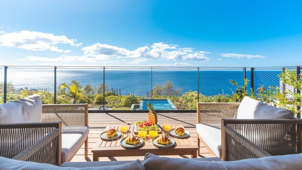 Eine Terrasse mit Korbmöbeln, einem Esstisch mit Speisen und Blick aufs Meer.