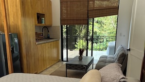 Ein Schlafzimmer mit Bett, kleinem Tisch, Sofa, Küchenbereich und Balkon mit Aussicht.