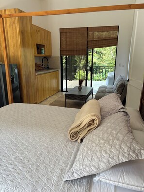 A bedroom with a bed, a small table, a sofa, a kitchen area, and a balcony with a view. - Brand-New Jungle Studios in Tamarindo! (Tamarindo)