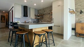 A modern kitchen with a central island, bar stools, a hanging light fixture, and a stone accent wall. - Sunset Waterfront Resort, Crown Jewel of Kelowna. Panoramic Lake Views, floor 18 (Kelowna)