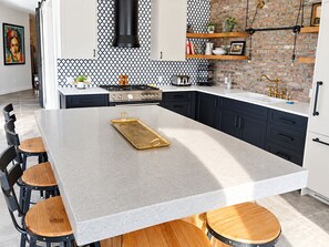 A modern kitchen with a large island, black cabinets, and a brick accent wall.
