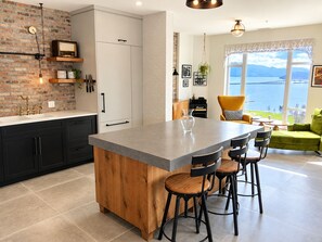 Una cocina moderna con una isla central, taburetes negros y vistas a un lago a través de grandes ventanales.