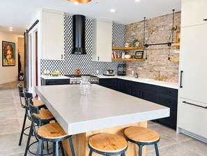 A modern kitchen with a large island, black cabinets, and a brick accent wall.