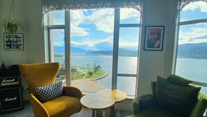 A living room with a large window, a yellow armchair, a green armchair, a small round table, and a Marshall amplifier. - Sunset Waterfront Resort, Crown Jewel of Kelowna. Panoramic Lake Views, floor 18 (Kelowna)