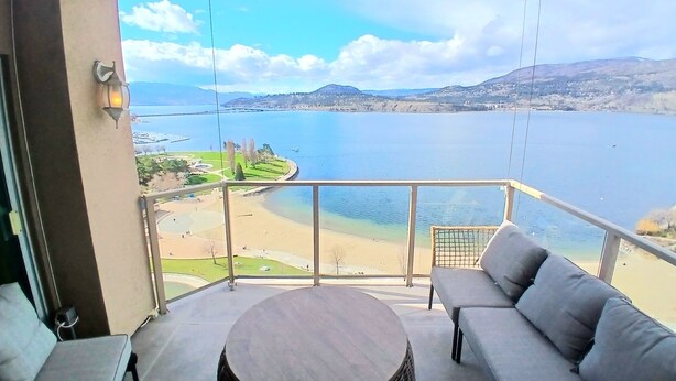 A balcony with a view of a beach and water, a round table, and two sofas. - Sunset Waterfront Resort, Crown Jewel of Kelowna. Panoramic Lake Views, floor 18 (Kelowna)