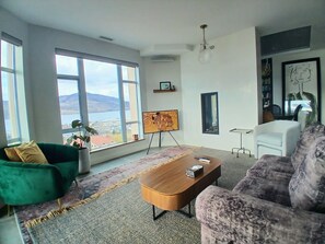 A modern living room with a large window, a green sofa, a purple sofa, a wooden coffee table, and a painting on the wall. - Sunset Waterfront Resort, Crown Jewel of Kelowna. Panoramic Lake Views, floor 18 (Kelowna)