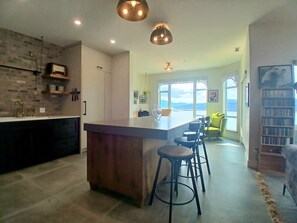 A modern kitchen with a central island, bar stools, and a view of the outdoors.
